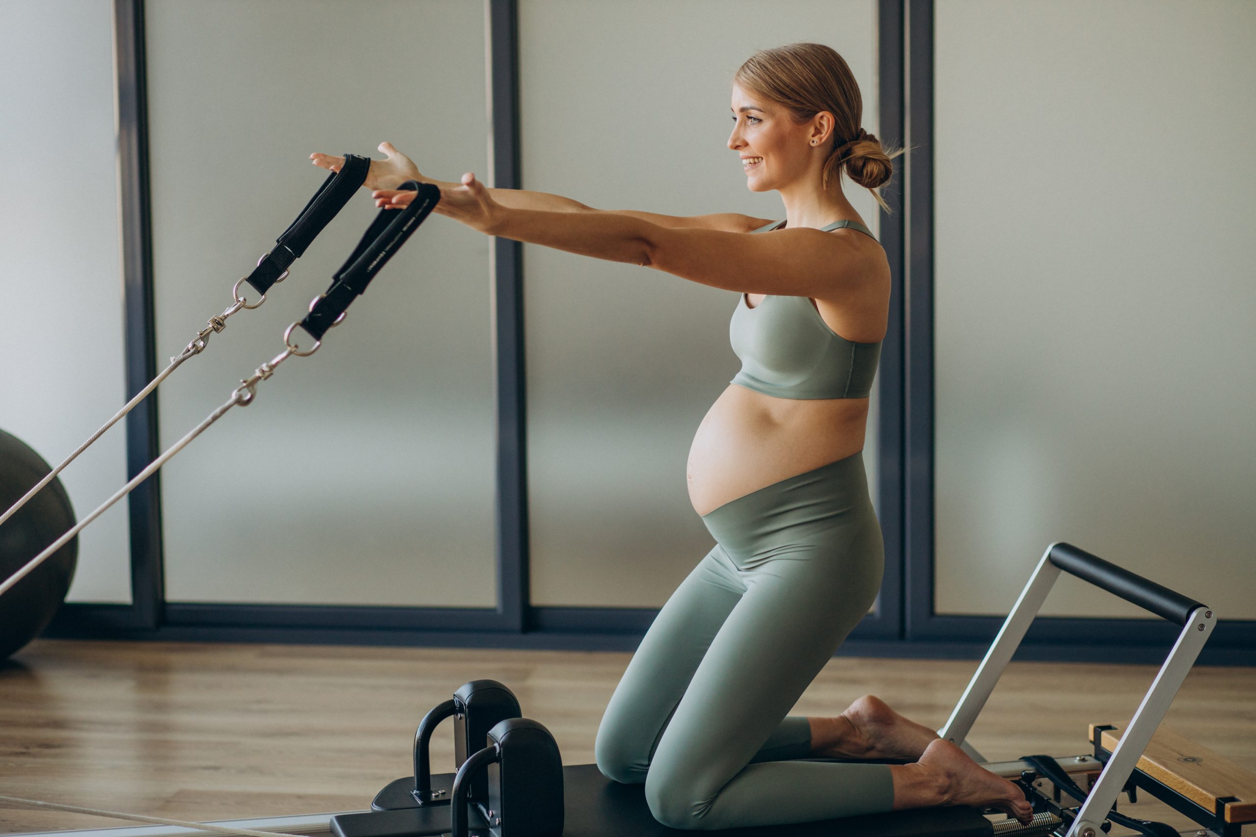 pregnant woman exercising with help reformer pilates class